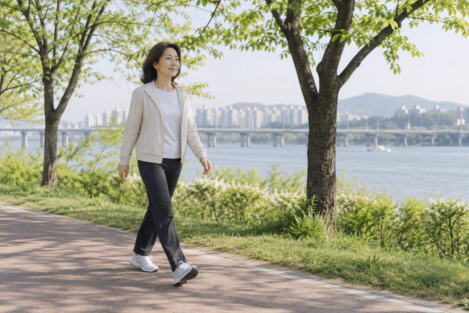 나무가 우거진 강변 길을 편안한 속도로 걷는 여성