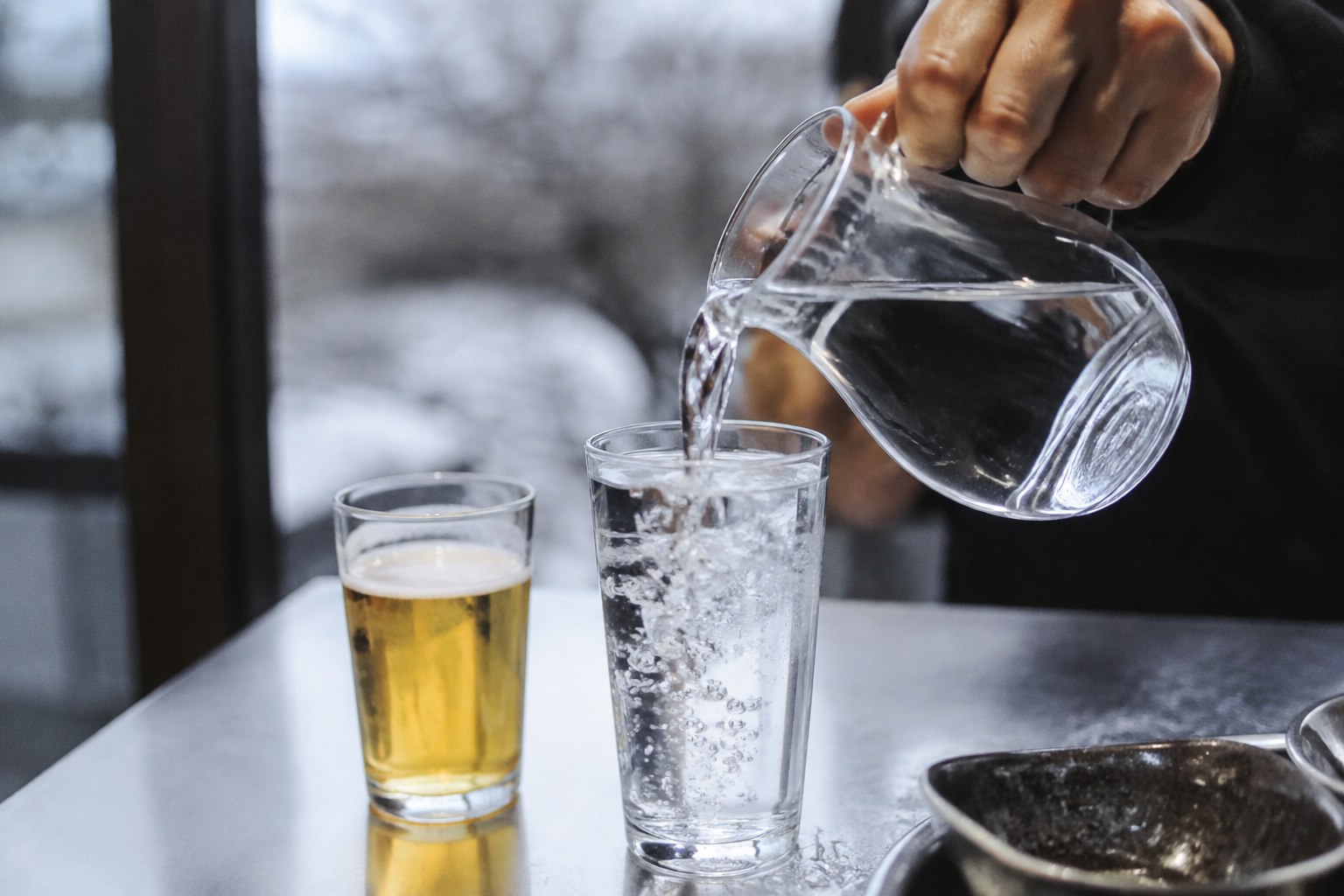 작은 맥주잔 옆 유리잔에 물을 따르는 손