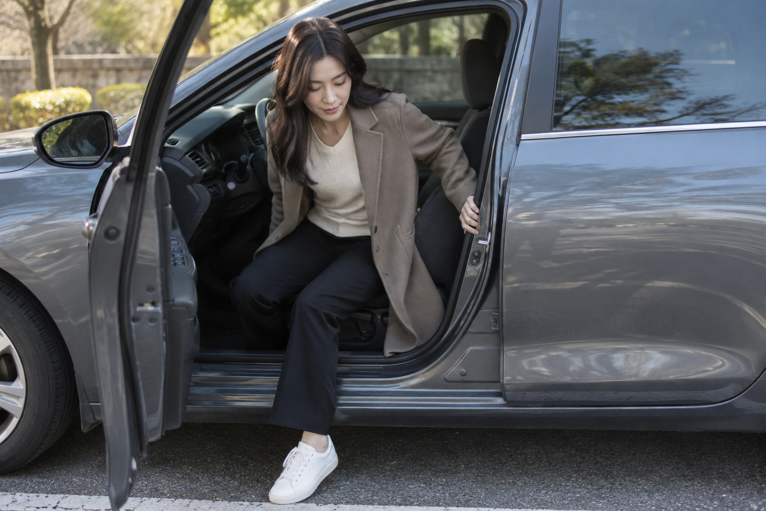 주차된 자동차에서 문틀을 잡으며 발을 바깥으로 내딛는 여성